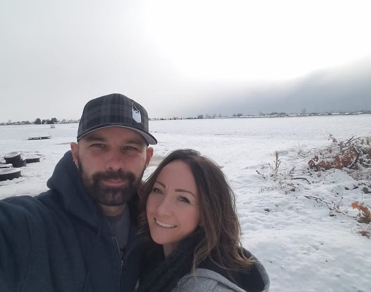 Tom and Sara, owners of Top Option Plumbing, smiling in a snowy field near their home in Caldwell, Idaho